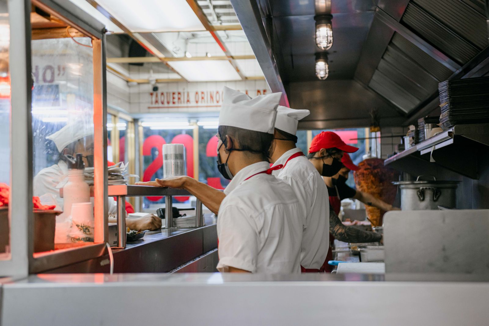 Culinary staff wearing uniforms and masks preparing meals in a bustling restaurant kitchen setting.