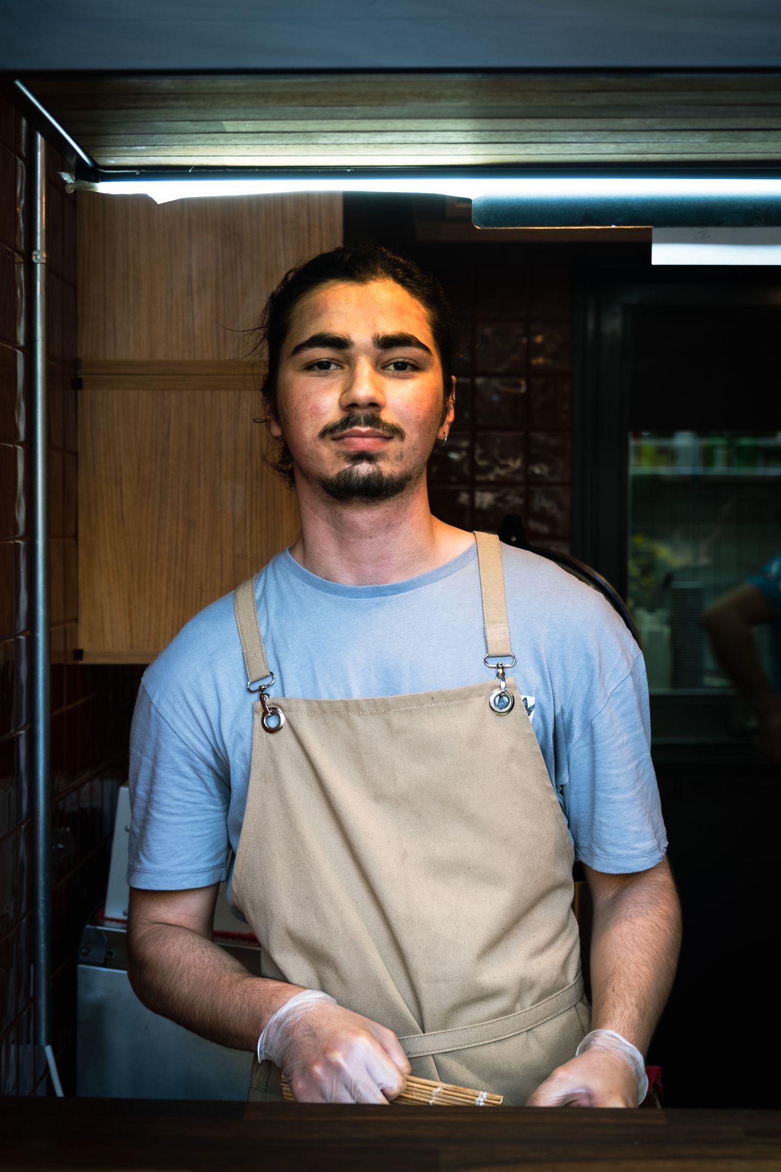 Portrait of a young chef standing confidently, wearing an apron, indoors.