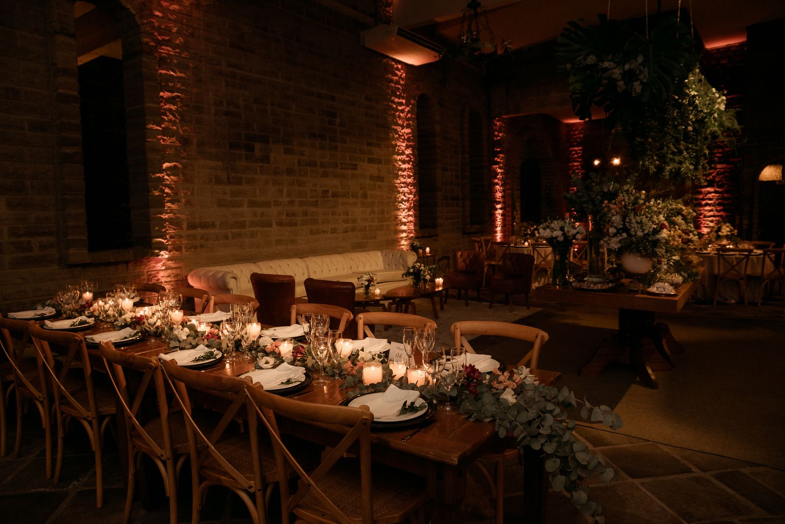 Warmly lit dining set-up in a decorated event hall with flowers and candles.