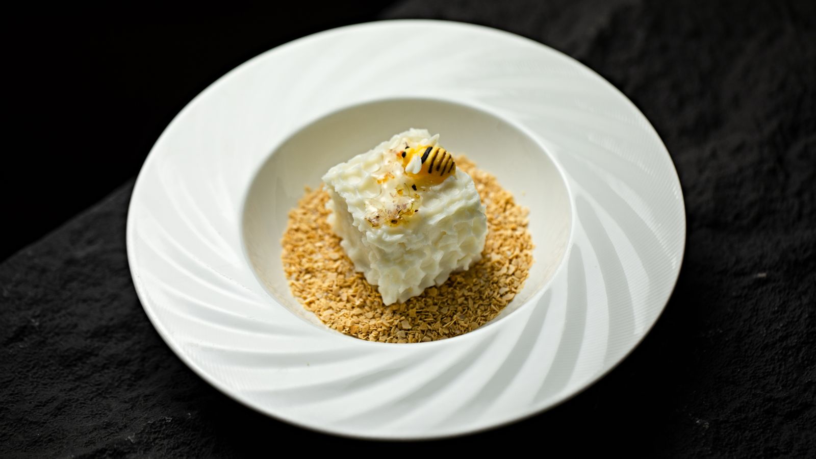 A delicious creamy dessert topped with honeycomb design on a crunchy base in a white dish.