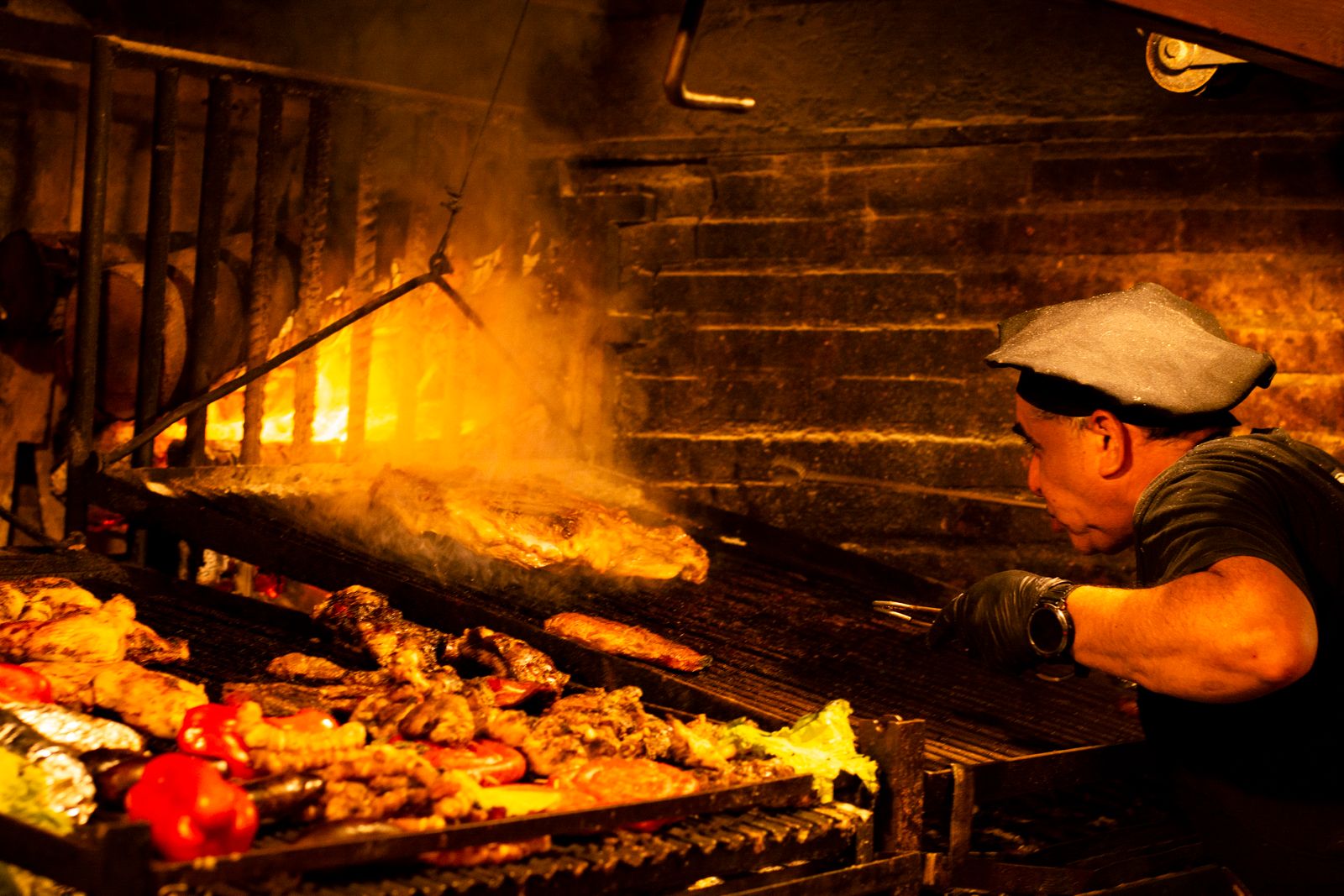 Chef prepares a traditional asado barbecue with sizzling meats over an open fire grill.